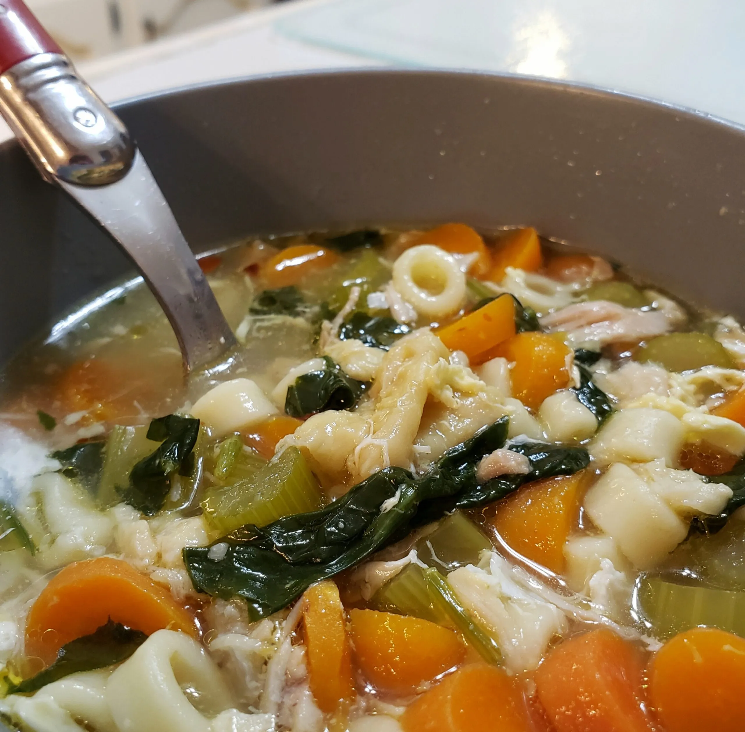 a bowl with a spoon full of chicken noodle soup with carrots and spinach